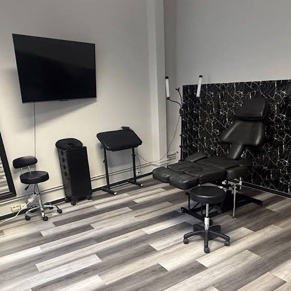 Tattooraum mit Liege, Stühlen und TV auf Holzboden.