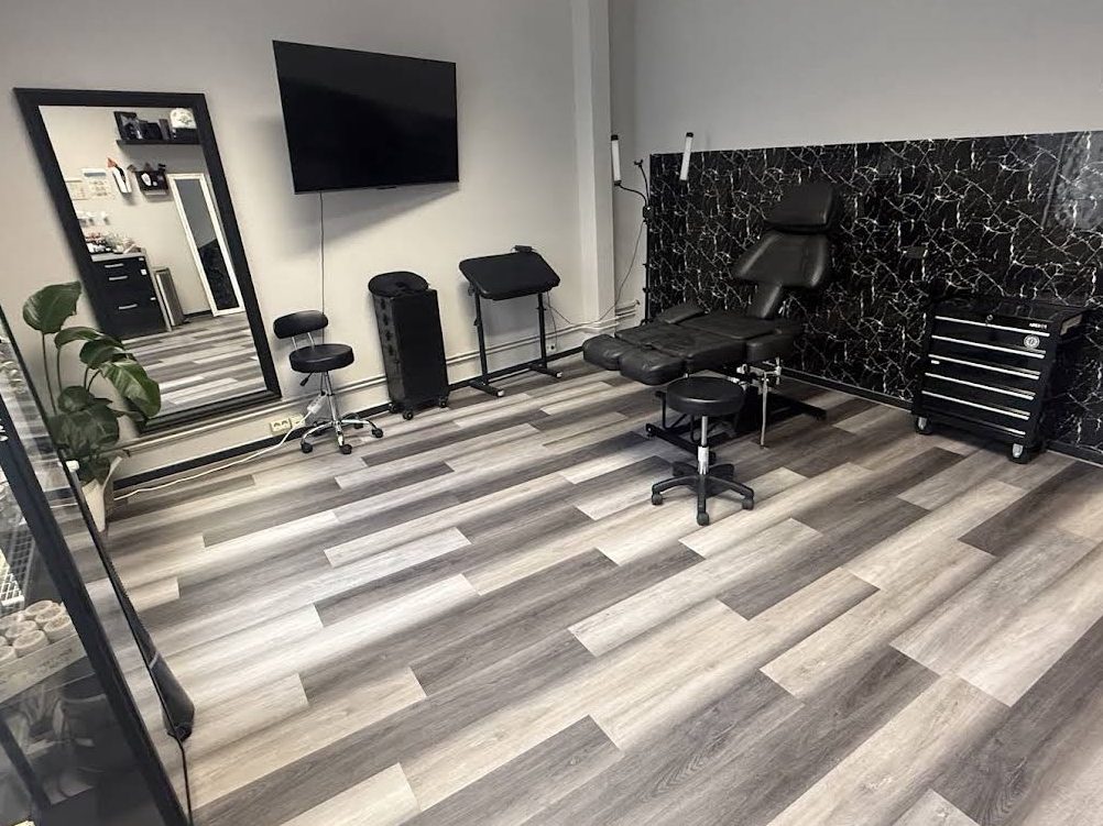 Tattoo-Studio mit Stuhl, Spiegel, TV und Holzfußboden.