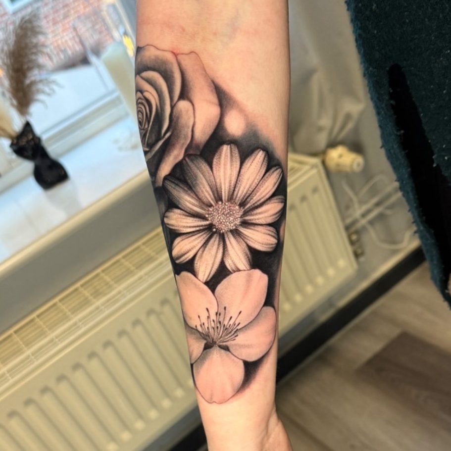 Tattoo auf dem Arm mit verschiedenen, detaillierten Blumenmotiven in Schwarz-Weiß.