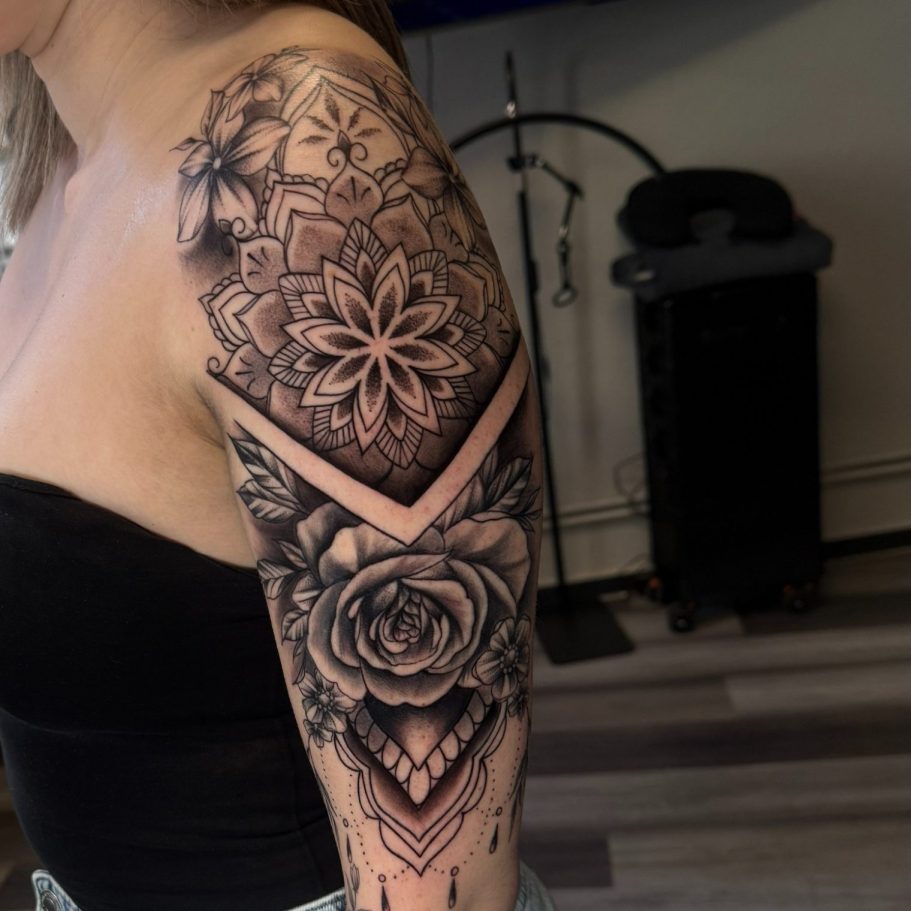 Schwarz-weiße Tätowierung mit geometrischen Mustern und einer Rose auf dem Oberarm.