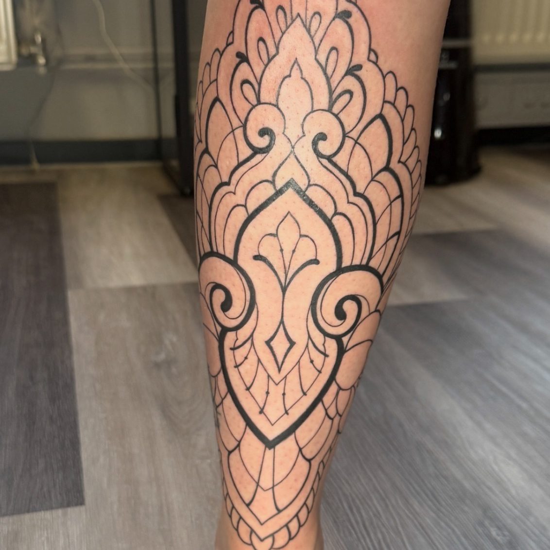 Schwarzes, filigranes Mandala-Tattoo auf dem Unterschenkel.