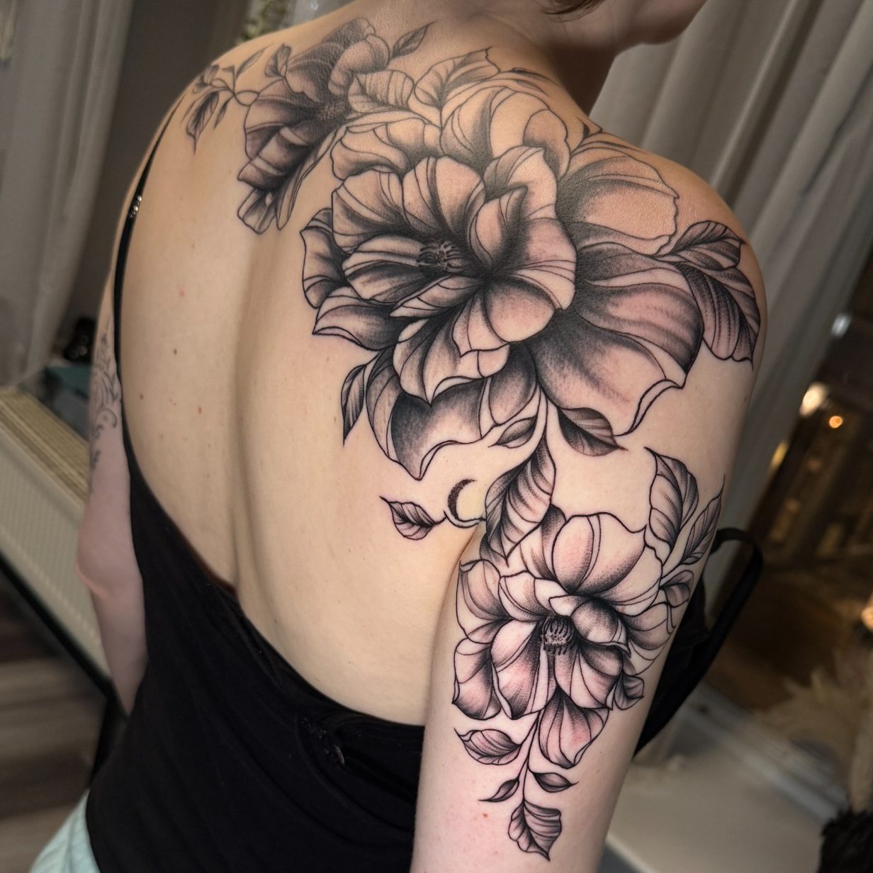 Schwarz-weiße Blumen-Tattoos auf dem Oberarm und Rücken einer Person.